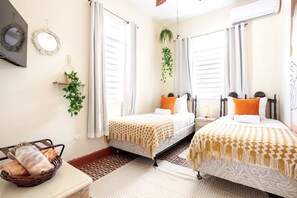 A hotel room with two beds, a TV, a mirror, a plant, and a basket of towels.
