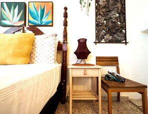 A bedroom with a bed, bedside table, lamp, chair, and artwork on the wall.