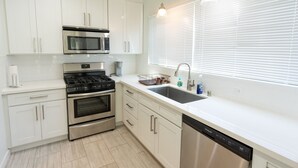 Una cocina moderna con armarios blancos, electrodomésticos de acero inoxidable, lavavajillas y una ventana con persianas.
