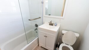 Un baño con ducha envuelta en vidrio, un lavabo blanco con un espejo encima y un inodoro.