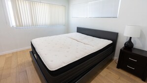 Un dormitorio con cama, una mesita de noche y dos ventanas con persianas.
