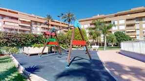Children can play on swings and a slide in this outdoor play area surrounded by a low wall.
