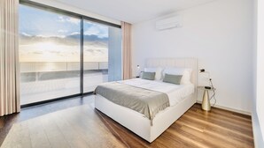 A modern bedroom with a large bed, a bedside table with a lamp, and a view of the sky through a large window. - Vila Cales e Chadas by Your Madeira Rentals (Arco da Calheta)