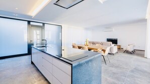 A modern kitchen with a central island, a dining area with a table and chairs, and a living area with a sofa and TV. - Vila Cales e Chadas by Your Madeira Rentals (Arco da Calheta)