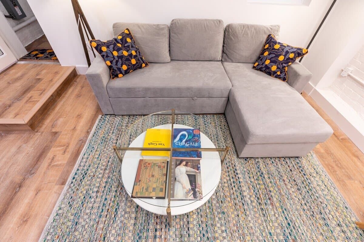 Uma sala de estar moderna com um sofá modular cinza, almofadas estampadas, uma mesa de centro com revistas e um tapete estampado.