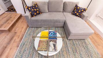Uma sala de estar moderna com um sofá modular cinza, almofadas estampadas, uma mesa de centro com revistas e um tapete estampado.