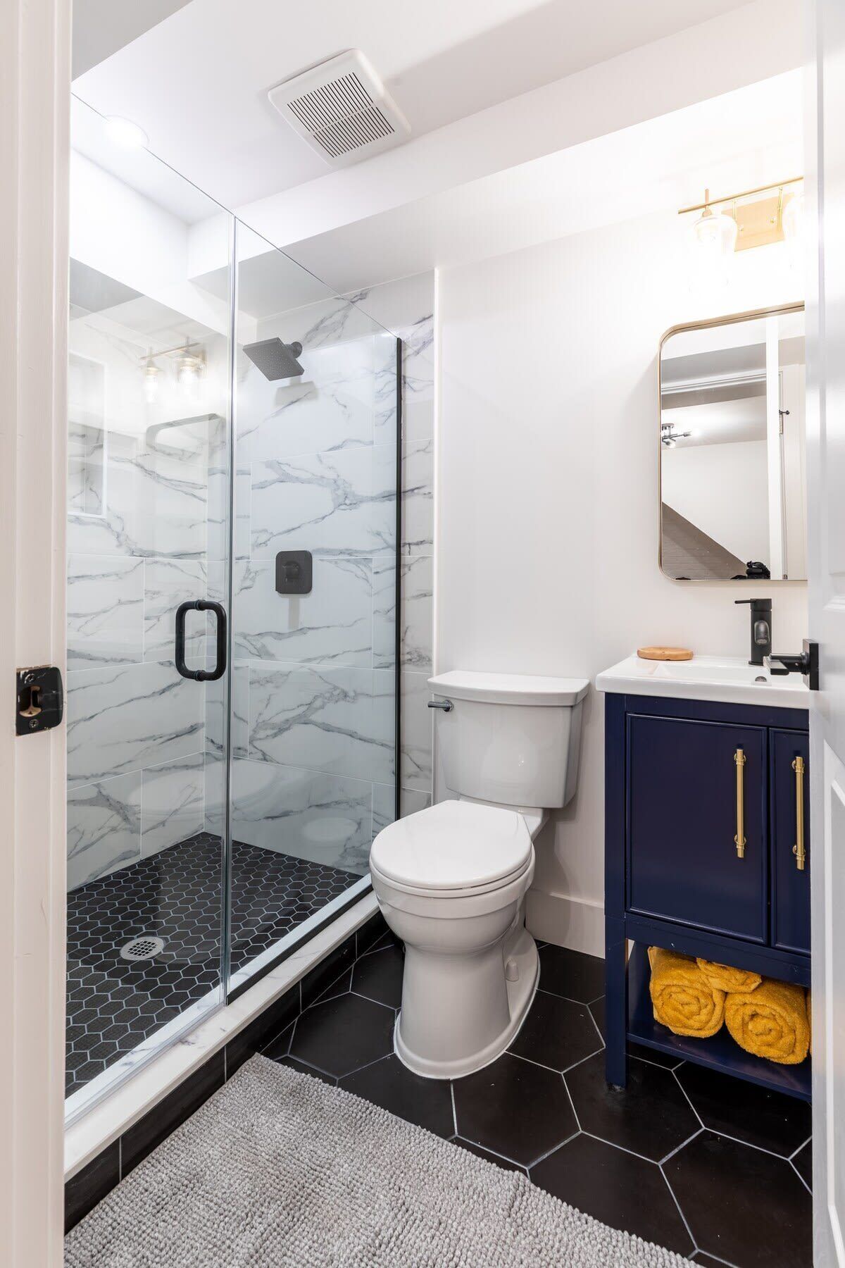 A modern bathroom with a glass shower enclosure, a white toilet, and a dark blue vanity with gold handles.