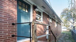 Ein Ziegelhaus mit blauer Tür, einer Holztreppe und einem Metallgeländer.