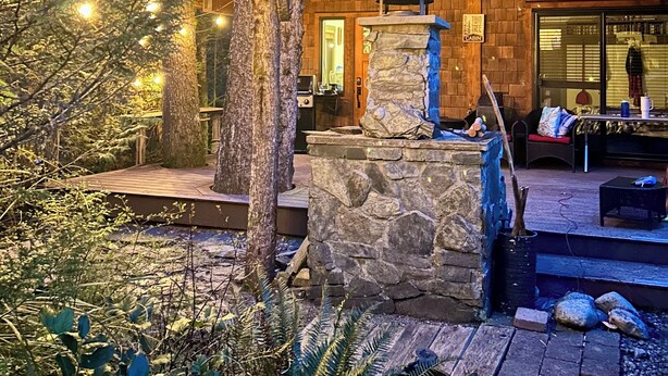Een chalet met een stenen open haard, houten terras en lichtjes.