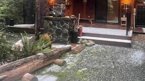 Een chalet met een stenen fundering, houten gevel en een veranda met treden naar een deur.