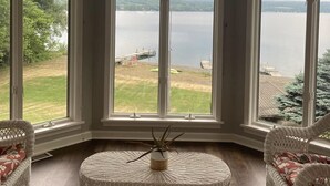 A room with large arched windows overlooking a lake, wicker furniture, and a small table with a plant. - Spacious multi-level lakeside home w/ renovated kitchen and abundant parking!  (Penn Yan)
