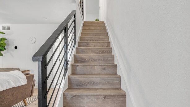 A staircase with wooden steps and a metal railing, leading to a bedroom with a bed and a plant. - Modern Townhome w/ Deck and Fast Wifi 7 min from AT&T Stadium  (Arlington)