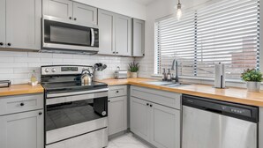 A modern kitchen with stainless steel appliances, grey cabinetry, and a wooden countertop. - Modern Townhome w/ Deck and Fast Wifi 7 min from AT&T Stadium  (Arlington)
