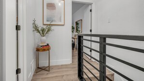 A hallway with a wooden floor, a black metal railing, a small table with a plant, and a framed picture on the wall. - Modern Townhome w/ Deck and Fast Wifi 7 min from AT&T Stadium  (Arlington)