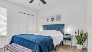 A bedroom with a bed, a bench, a nightstand, a potted plant, and a window with blinds. - Modern Townhome w/ Deck and Fast Wifi 7 min from AT&T Stadium  (Arlington)