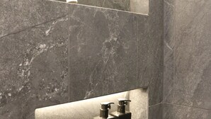 Une salle de bain avec des carreaux de marbre gris, un miroir et deux articles de toilette noirs posés sur une étagère.