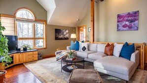 A cozy living room with a large window, a sofa, a coffee table, and a television. - The Kebler Home: Walk to Elk Ave! Dog Friendly! (Crested Butte)