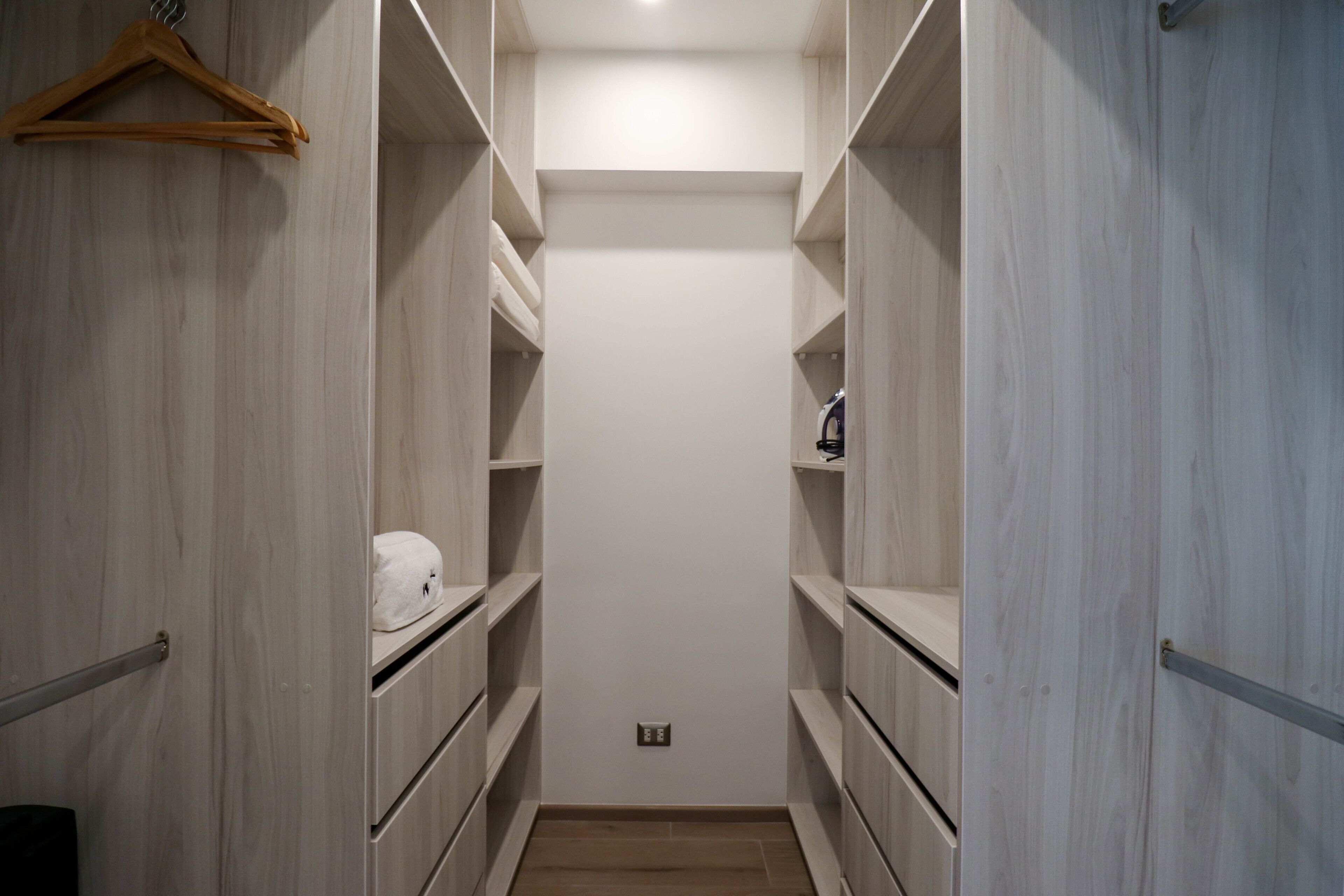 A narrow walk-in closet with wooden shelving and a hanging rack.