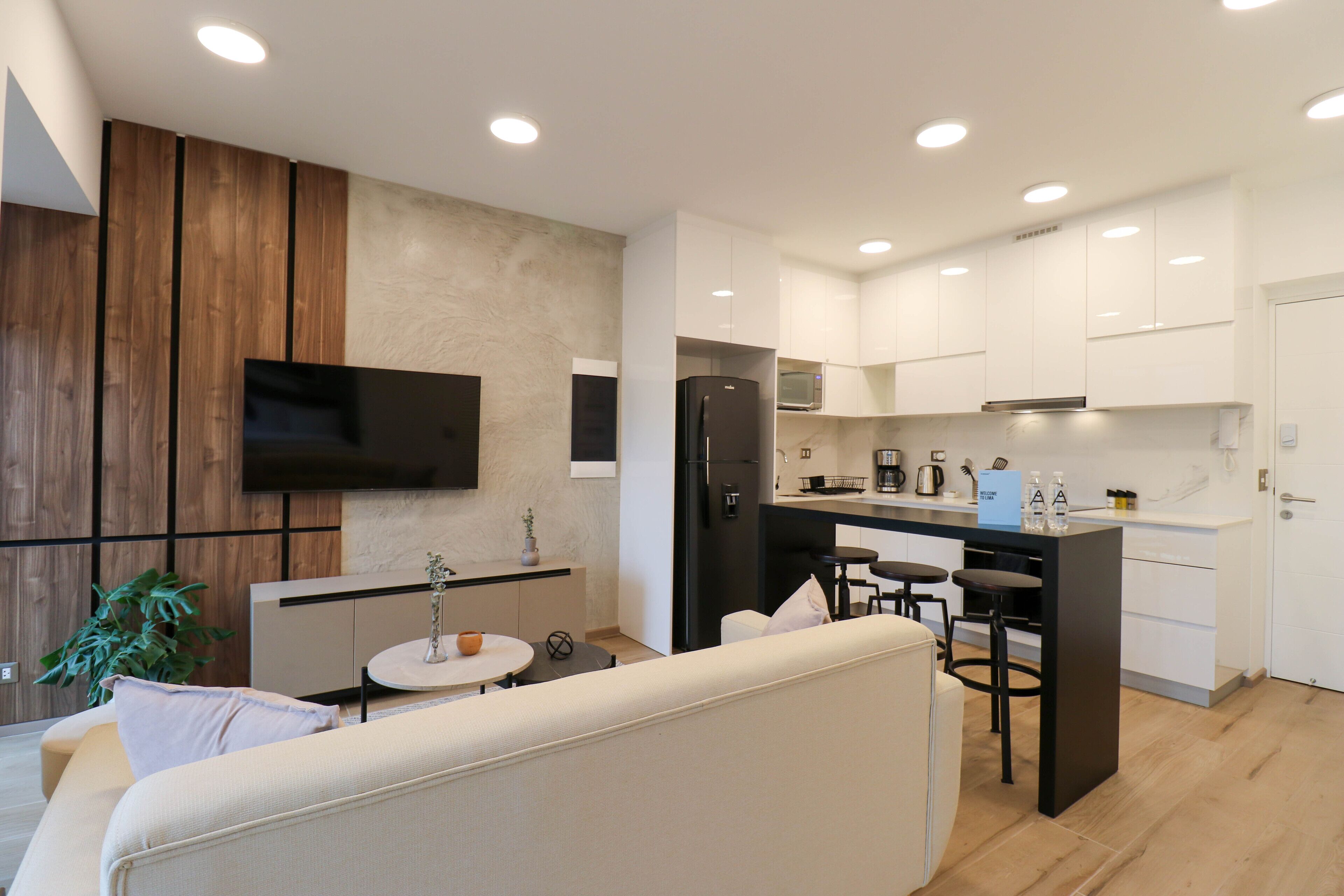 A modern kitchen with white cabinets, a black refrigerator, and a built-in microwave. There is a small island with bar stools and a round table with a vase and a bowl.