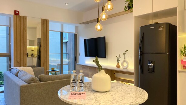 A modern living room with a sofa, a round marble table with bottles, a TV, and a black refrigerator.