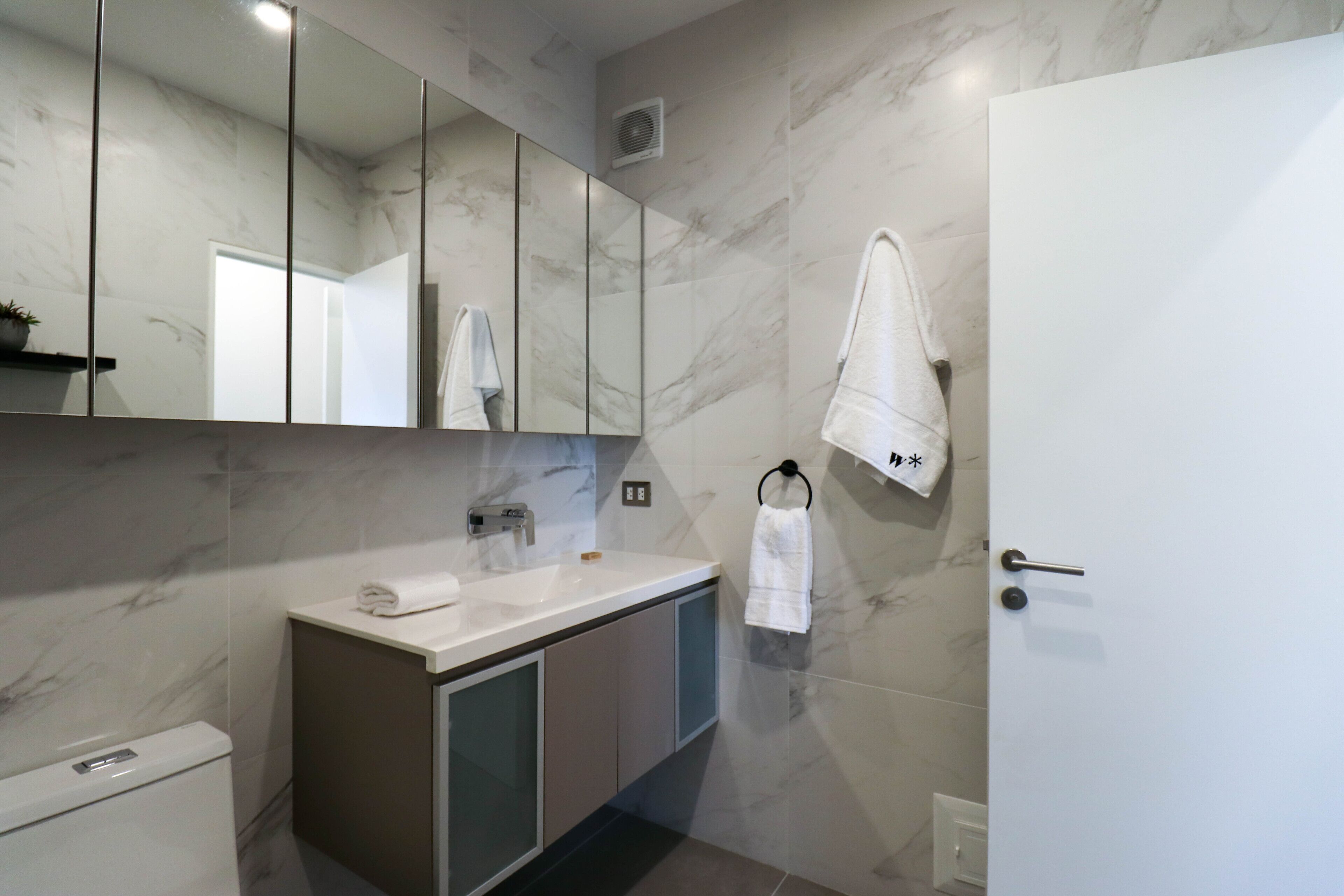 Un baño moderno con salpicadero de mármol, un espejo grande, un lavamanos con una toalla y una puerta.