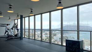 A gym with large windows, exercise equipment, and a view of a cityscape.