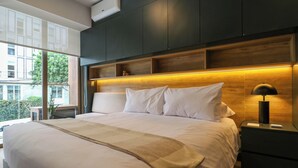 A modern bedroom with a large bed, built-in shelving, and a bedside table with a lamp.