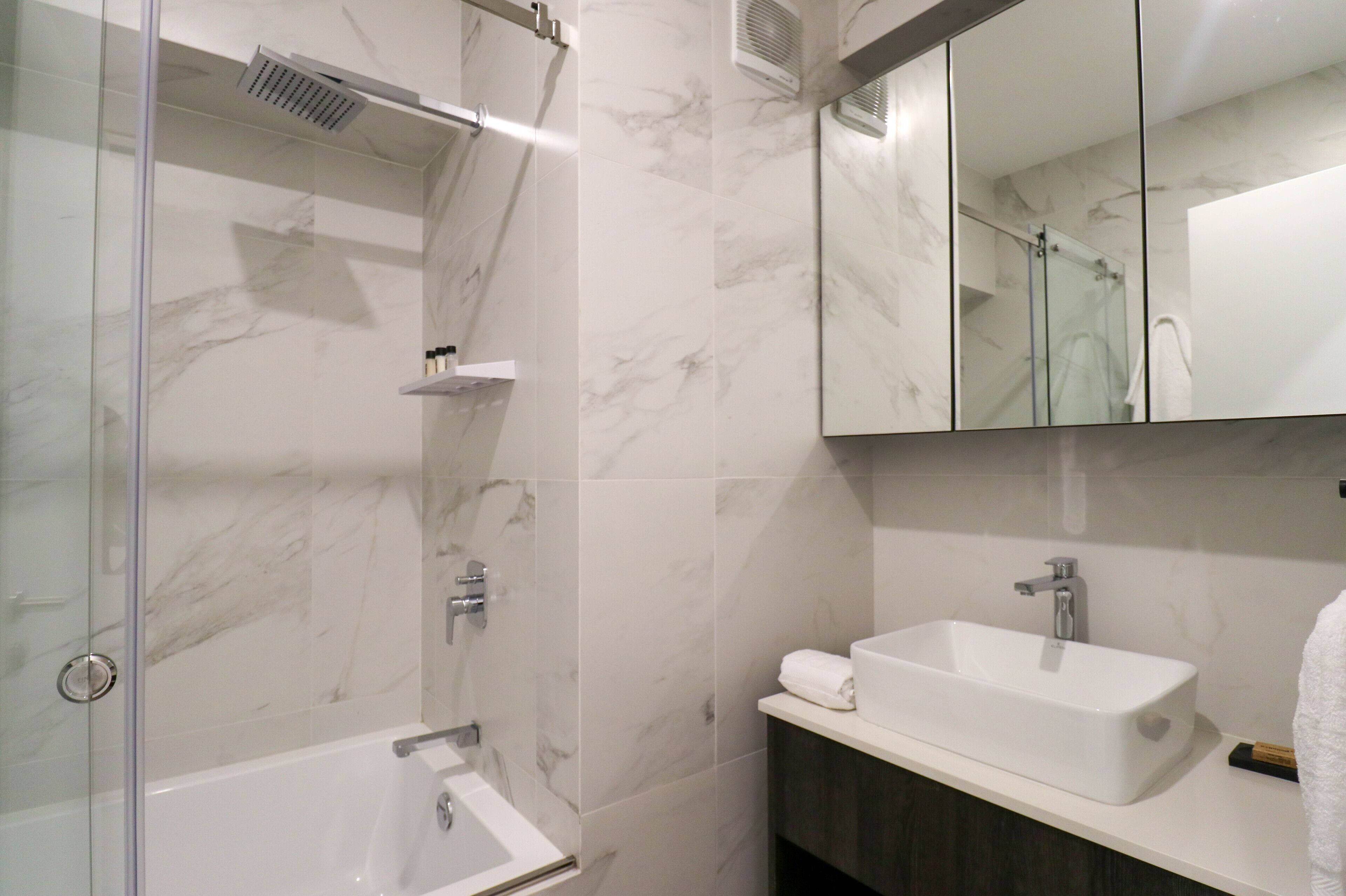 A modern bathroom with a glass-enclosed shower, a white sink, and a large mirror above the sink.