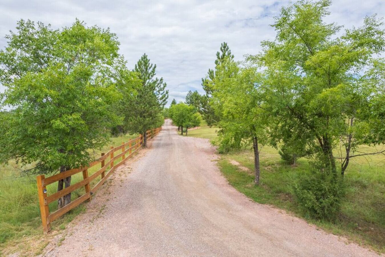 Un camino de grava bordeado por vallas de madera y árboles.