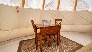 L’intérieur d’une tente, avec une table en bois, des chaises et un tapis tissé.