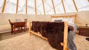 L’intérieur accueillant d’une tente ronde, avec un lit, une table en bois et des chaises.