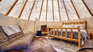 En hyggelig indretning i en yurts med seng, sofa og et lille skrivebord med en computer.