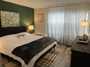 A hotel room with a bed, a nightstand, a lamp, a framed quote on the wall, and a window with curtains. - 
Newly Updated Modern, Spacious, and Cozy Condo- Right on the Lake! (Lake Geneva)