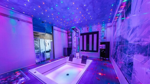 A spa room with a large bathtub, a massage table, and a ceiling with colorful lights.
