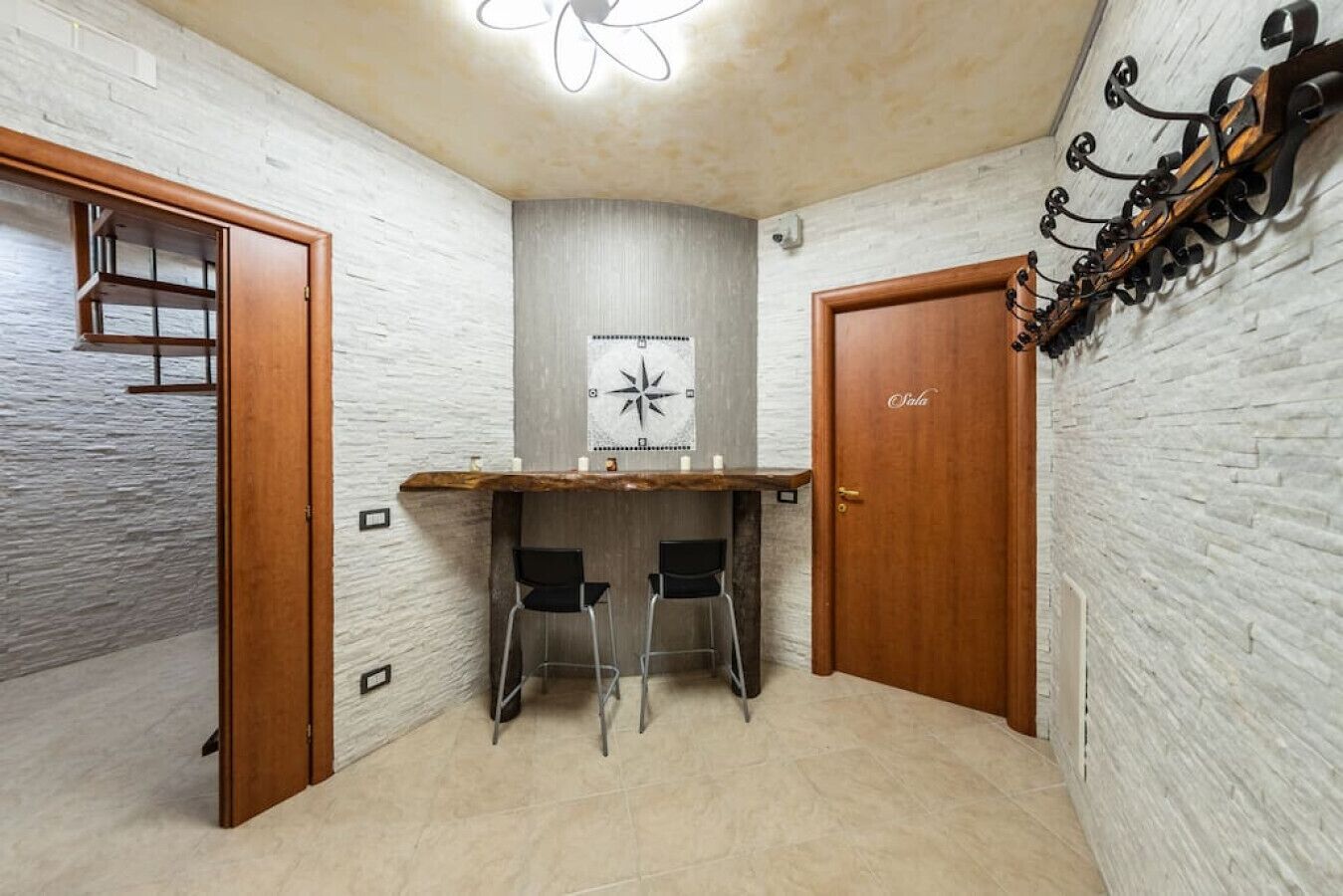 A corner room with a wooden door, a white brick wall, a ceiling fan, and a bar area with two stools.