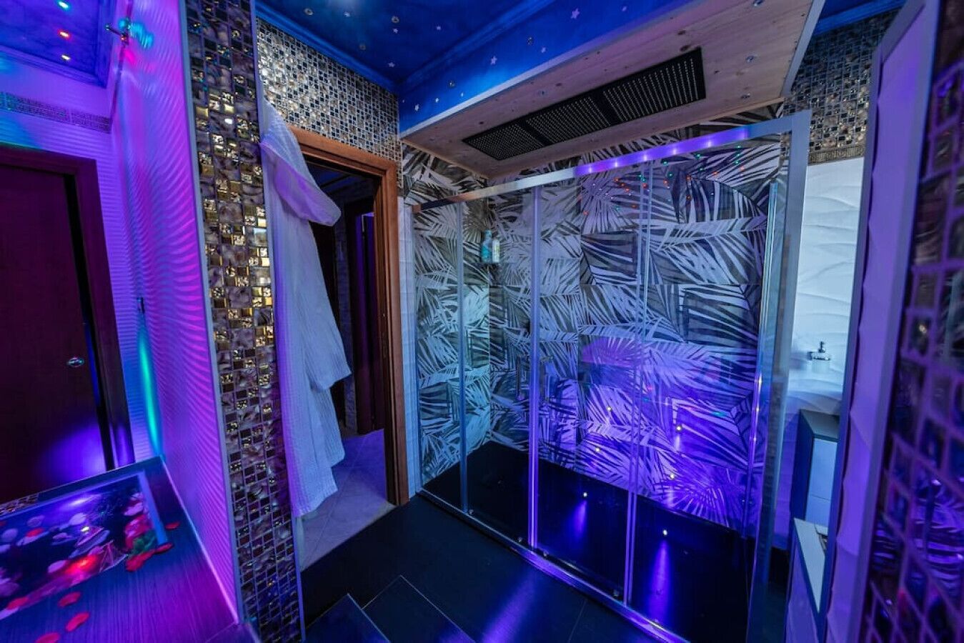 A modern bathroom with a glass shower enclosure, a wooden door, and a starry ceiling design.
