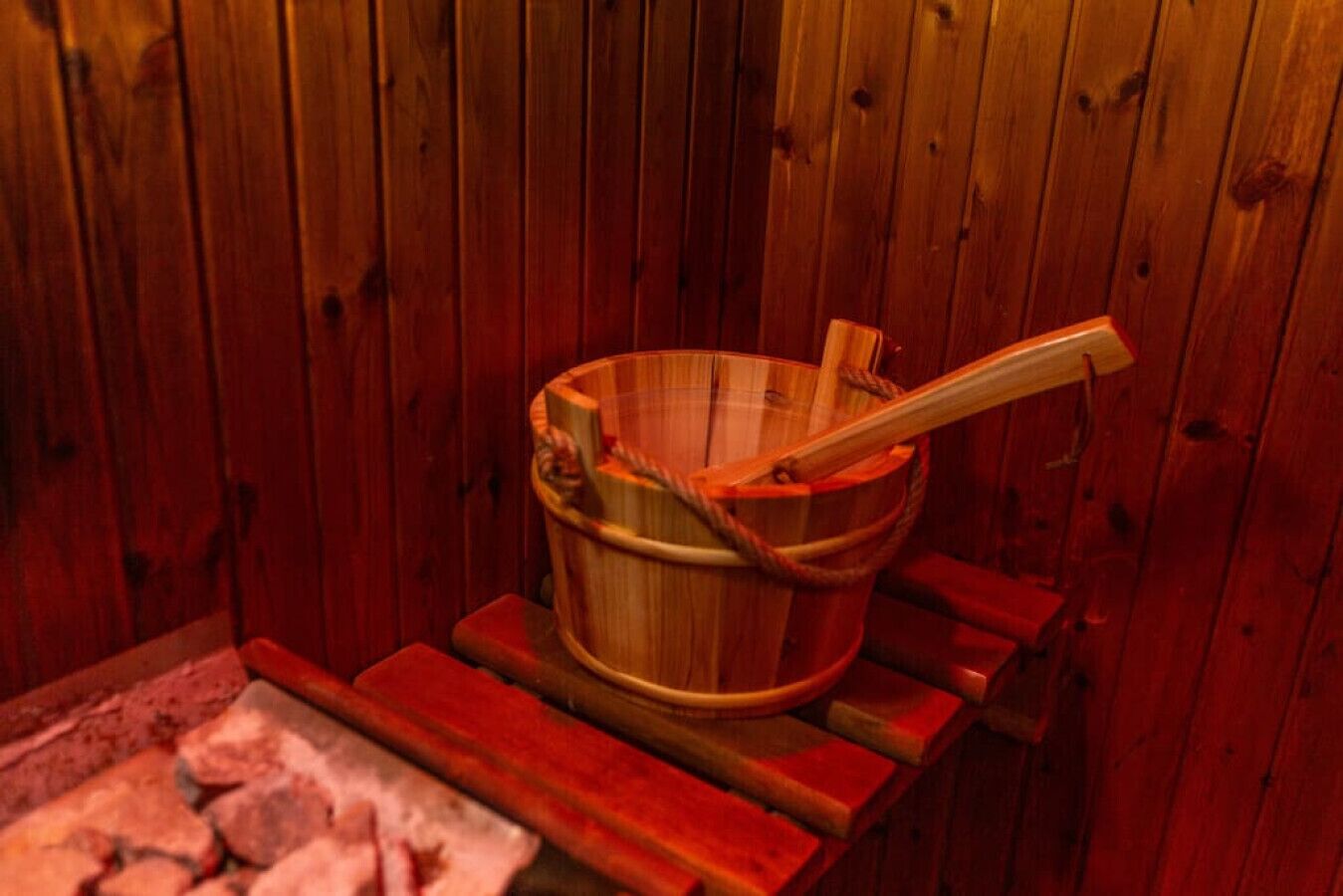 Un sauna avec un seau en bois et une louche en bois sur un banc en bois.