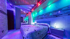 A modern bedroom with a large bed, a nightstand, and a wall-mounted lamp.