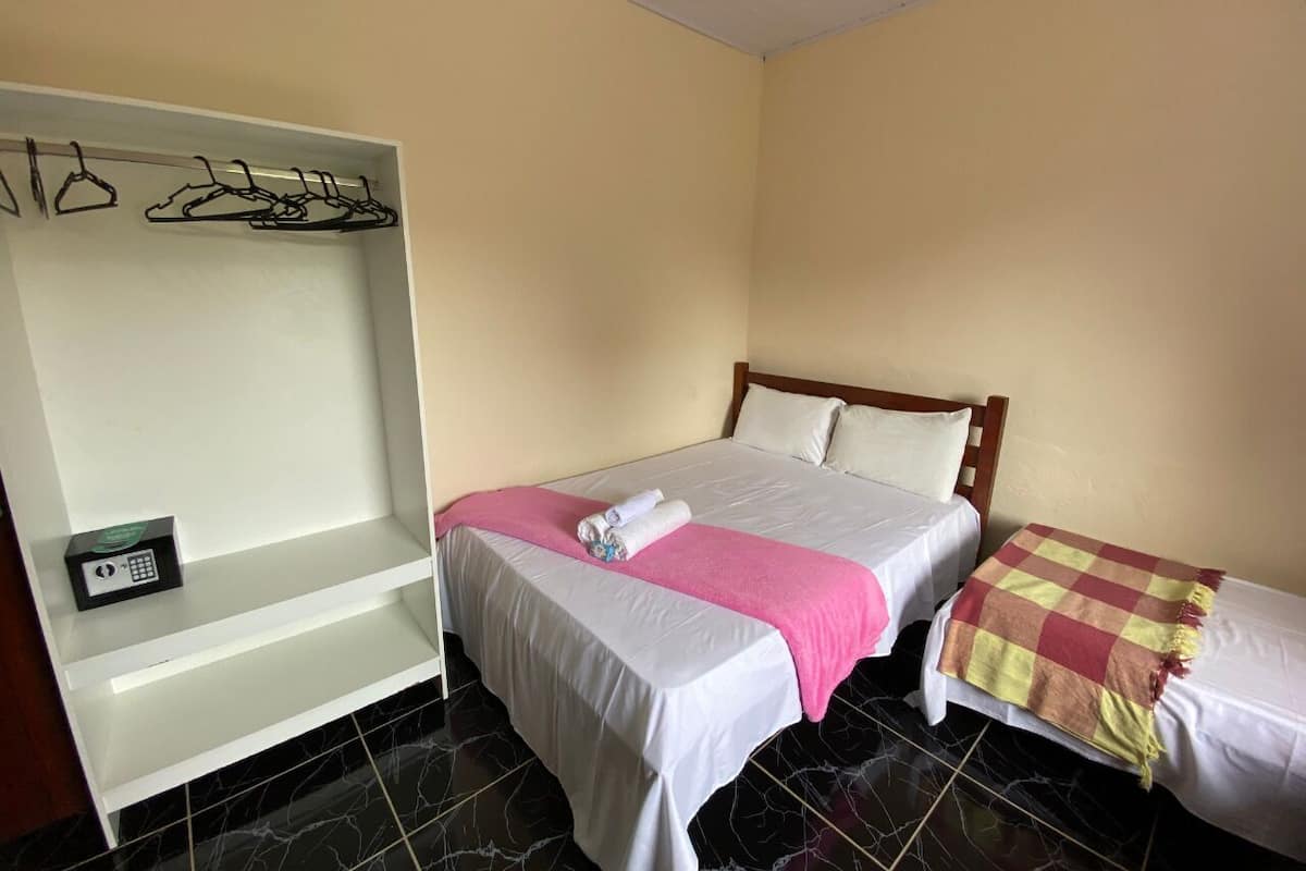 A hotel room with a bed, a bench with hangers, and a small safe.