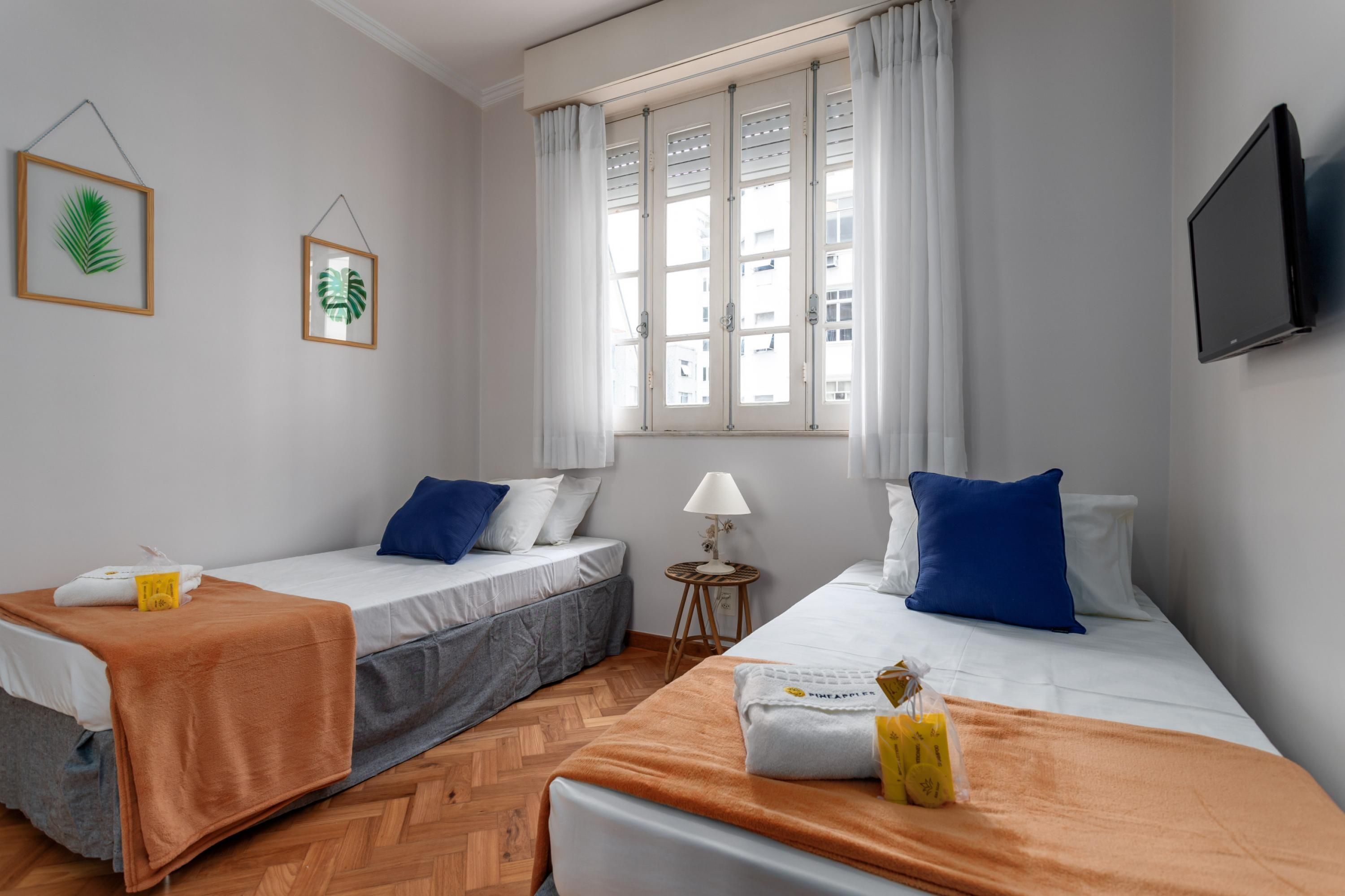 A hotel room with two beds, a TV, a window with curtains, and framed leaves on the wall.