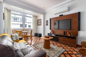 A modern living room with a large flat-screen TV, wooden furniture, and a patterned floor. - Sea View 2 Minutes From the Beach Fms502 (Rio de Janeiro)