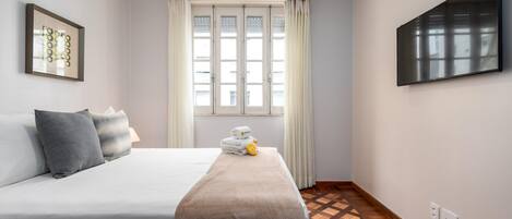 A hotel room with a bed, a TV mounted on the wall, a window with curtains, and a patterned floor.