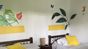 A hotel room with two beds, each with white bedding and a yellow pillow. There is a nightstand with a lamp and a small table between the beds. The walls have decorative wall art featuring flowers and butterflies. - CASA HOTEL MÁLAGA (Montenegro)