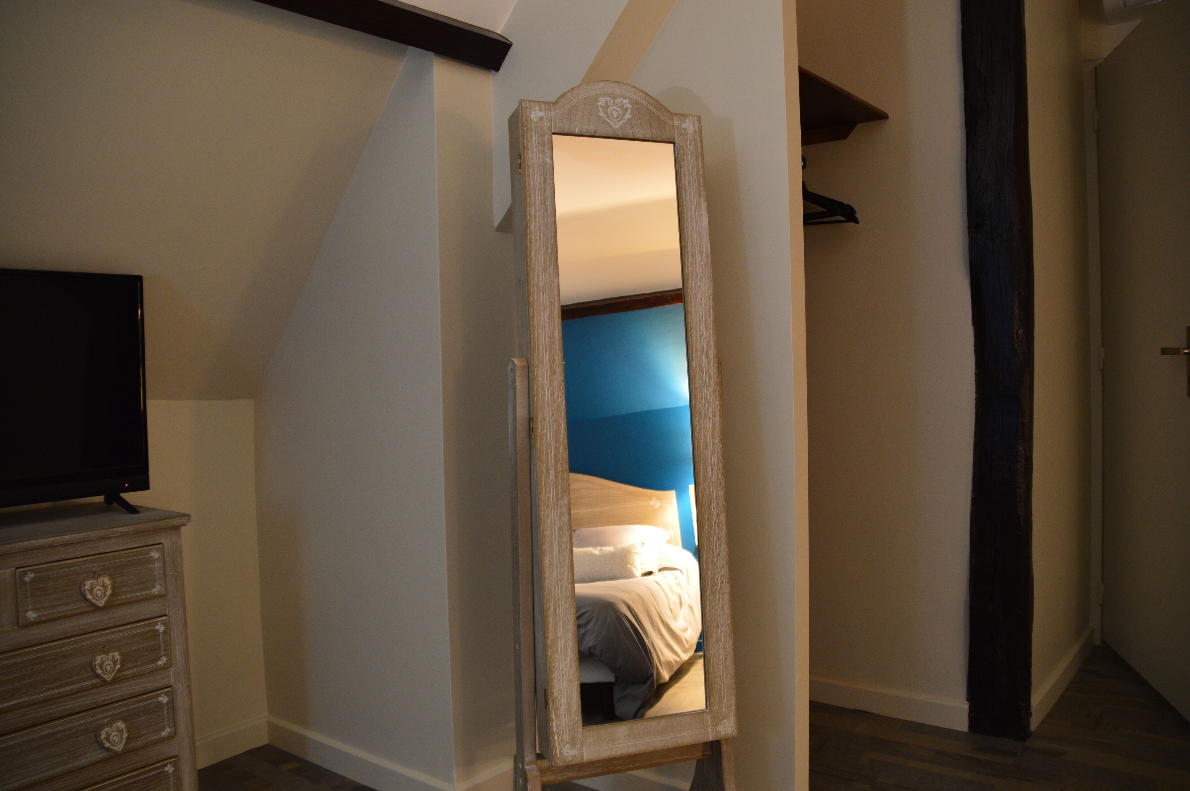 Une chambre avec un grand miroir, une commode aux poignées en forme de cœur, un lit avec une literie blanche et un mur d’accent bleu.
