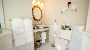 Une salle de bain avec un sol en marbre, un miroir encadré d’or, des toilettes blanches et une commode dorée.