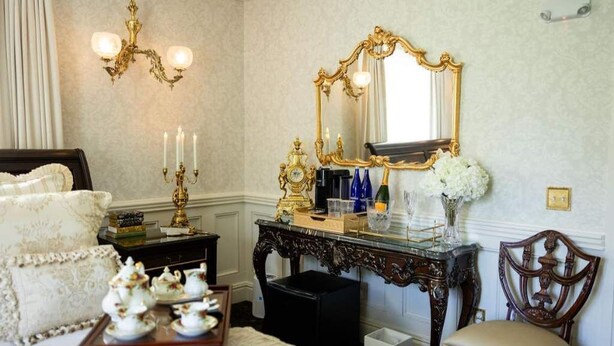 Une chambre classique, élégamment meublée, avec un grand lit, des meubles richement décorés et un miroir doté d’un cadre doré.