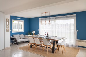 A modern dining area with a large table set for four, surrounded by white chairs.