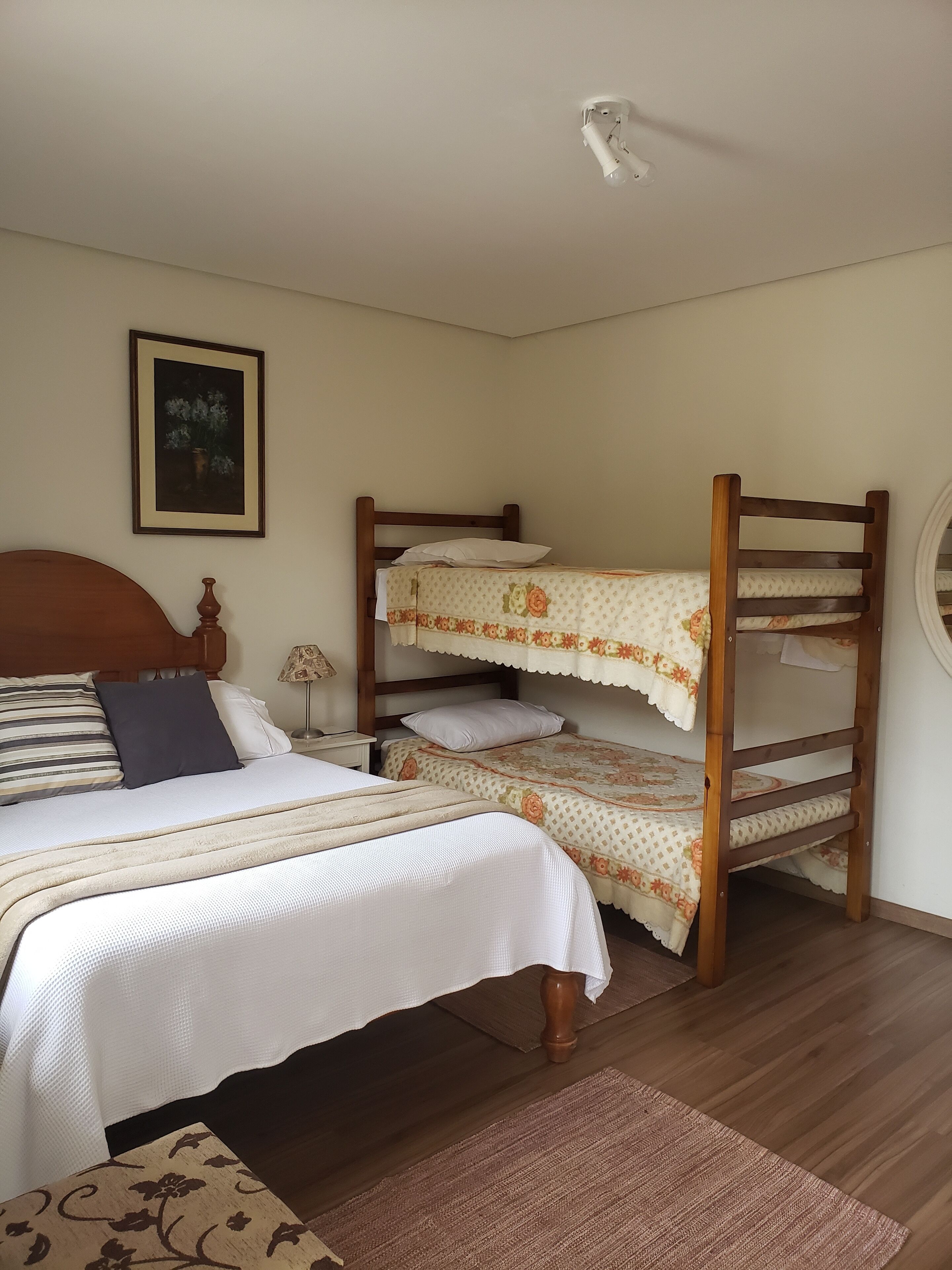 Un dormitorio con una cama individual, una cama nido de madera, una mesita de noche con una lámpara y un cuadro enmarcado en la pared.