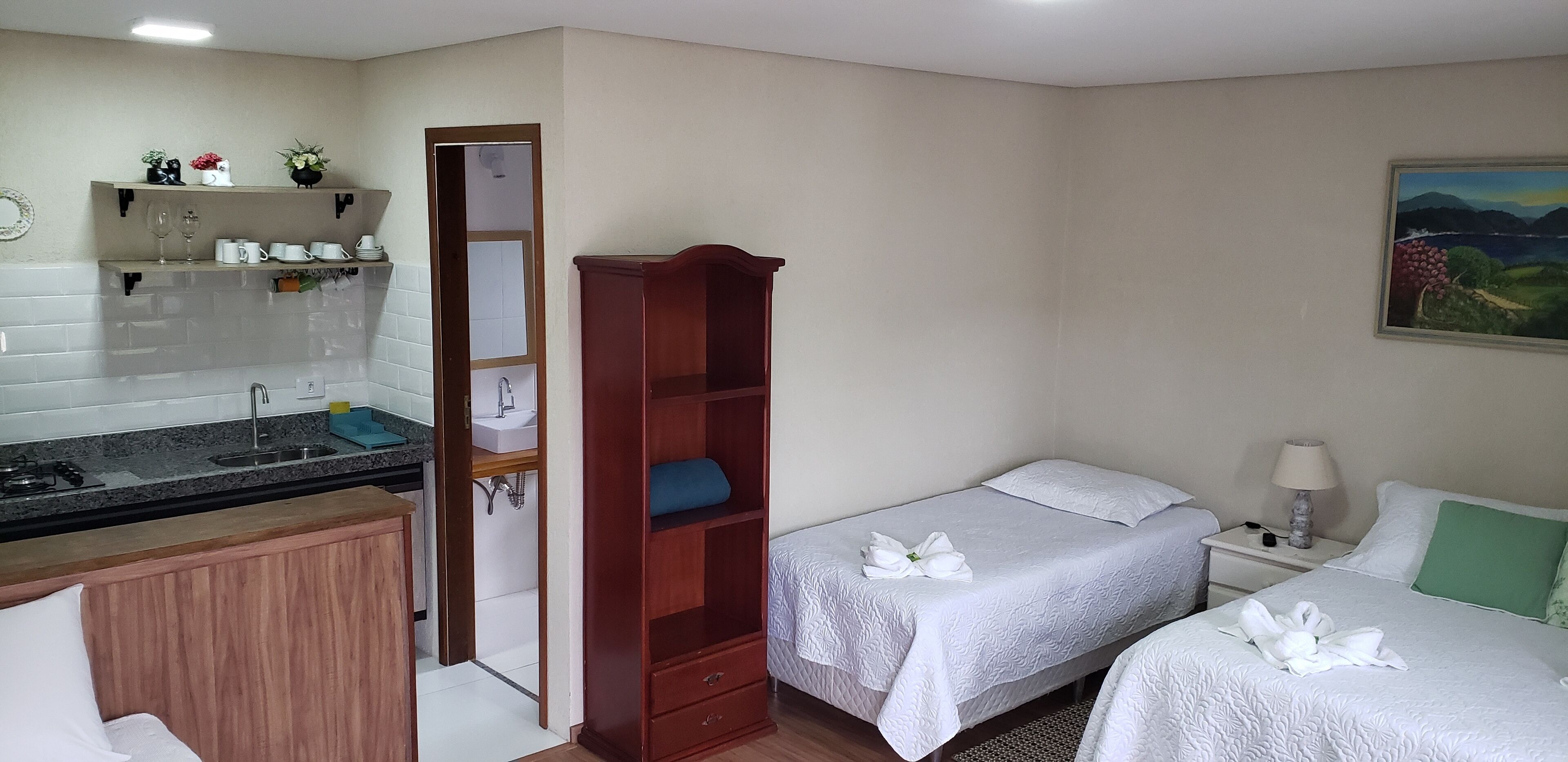 Une chambre d’hôtel avec une kitchenette, deux lits avec du linge de lit blanc, une armoire en bois et un tableau au mur.