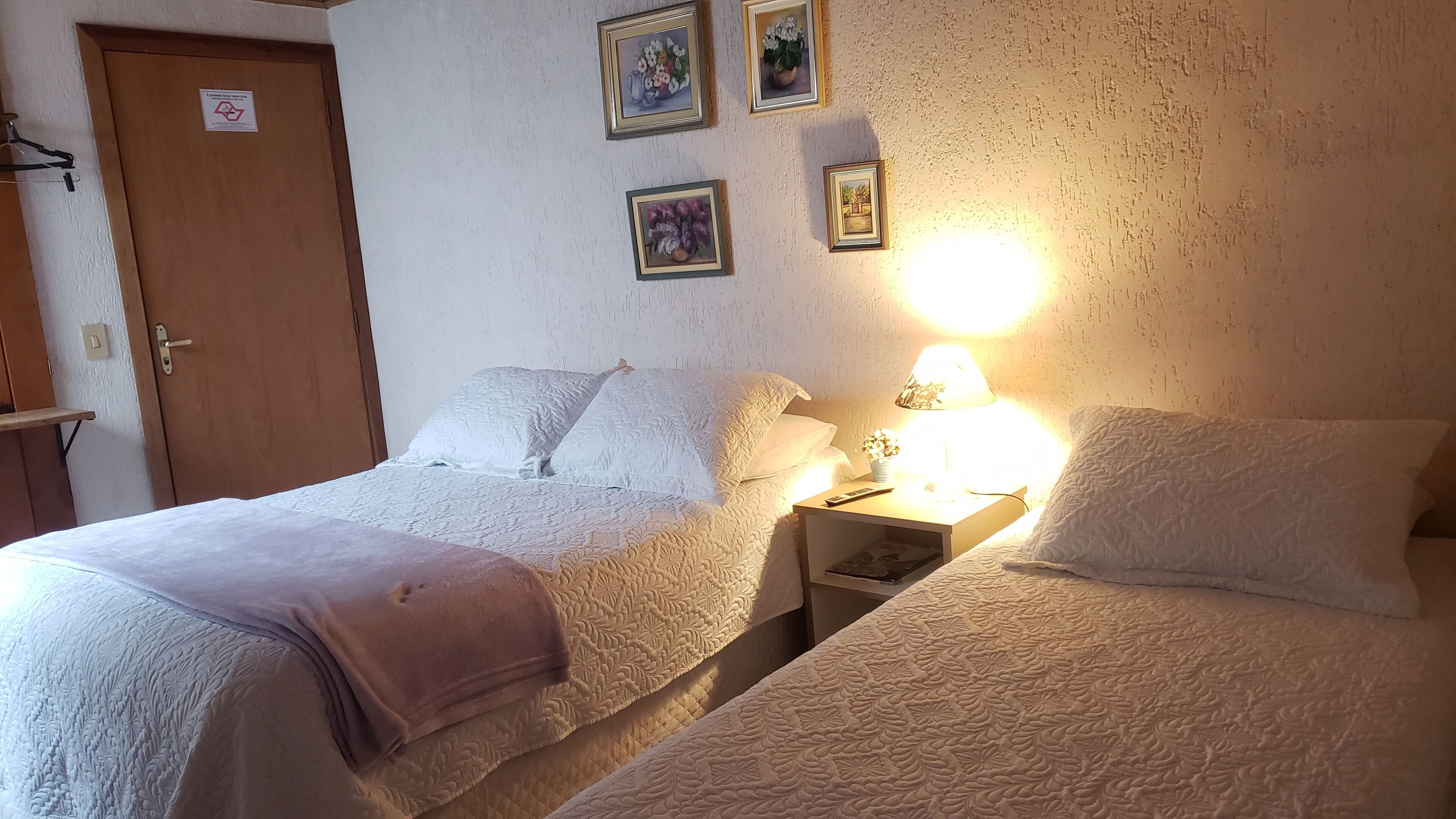 Ein Zimmer mit zwei Betten, einem Nachttisch mit Lampe und einer Tür mit einem Schild.